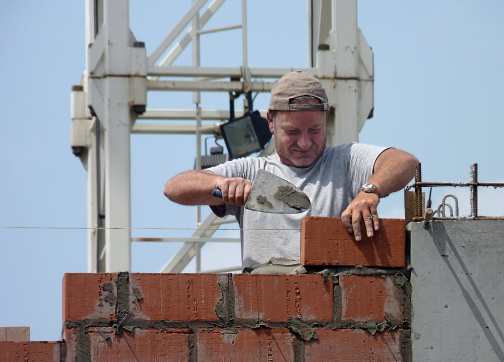Albañil con cuchara colocando ladrillos en un muro de obra
