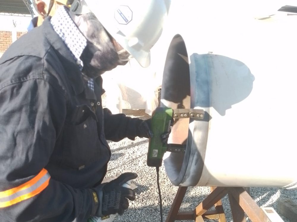Operador con respirador preparando la superficie de una tubería antes del recubrimiento
