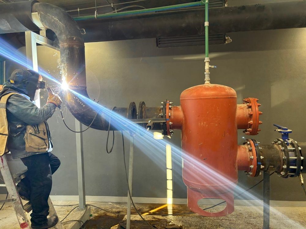 Soldador trabajando en tubería junto a un recipiente de proceso